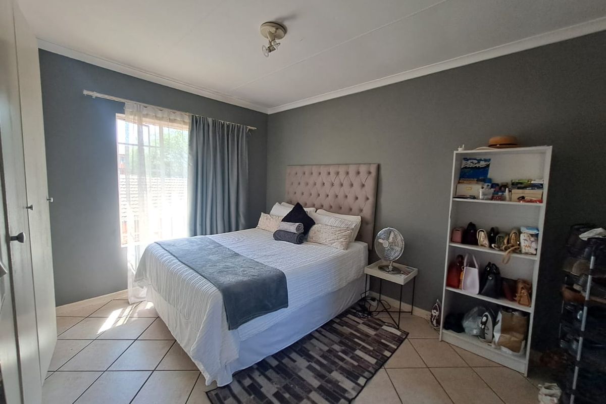 A well-lit bedroom featuring tiled flooring, a built-in cupboard, and neutral grey wall finishes, providing a comfortable and functional living space.