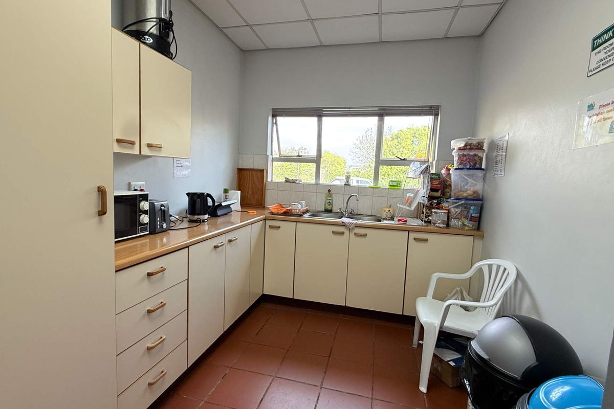 A functional office kitchenette featuring laminate countertops, built-in cabinetry, a stainless steel sink, and a drop ceiling.