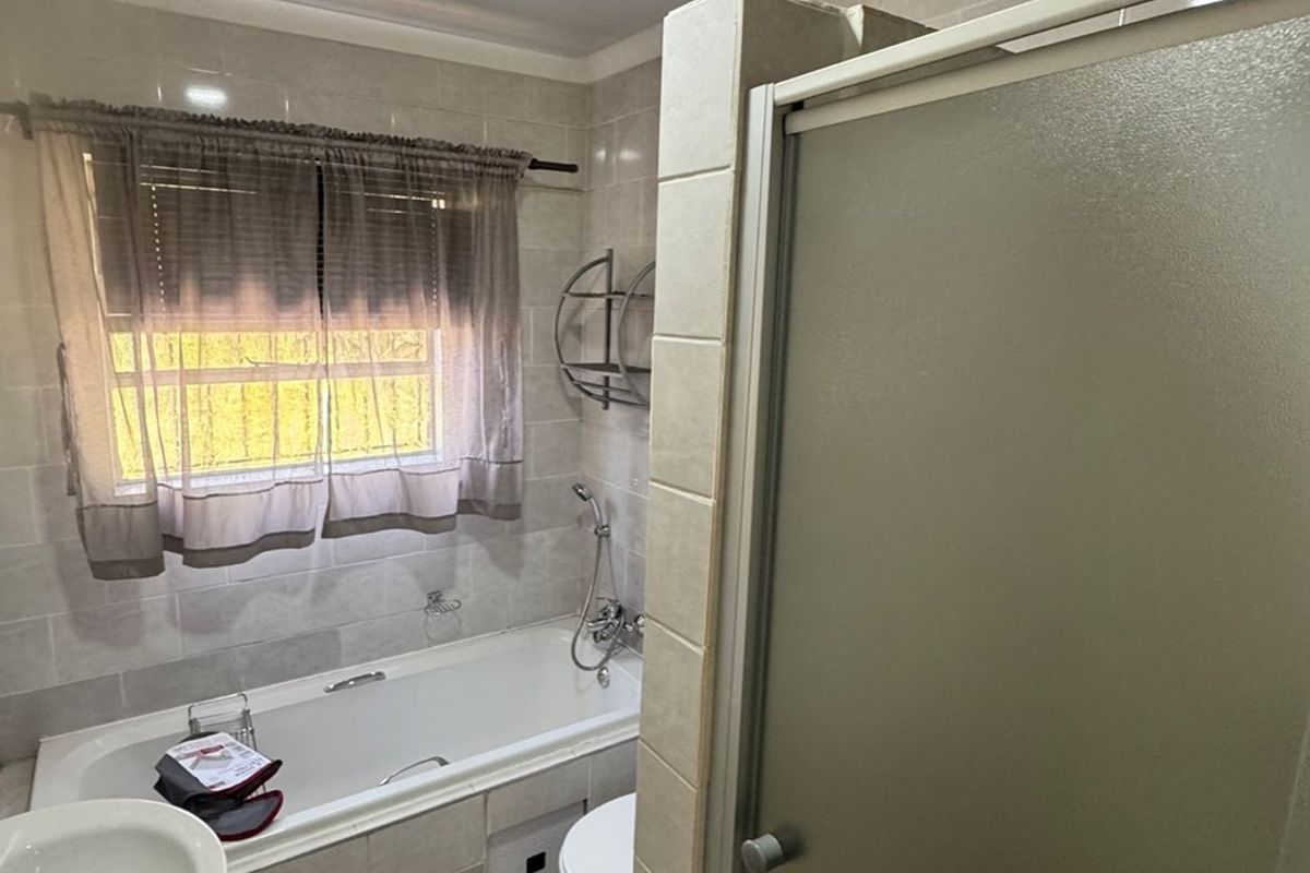A functional bathroom featuring a bathtub, separate shower enclosure, pedestal basin, and toilet with neutral wall and floor tiling.