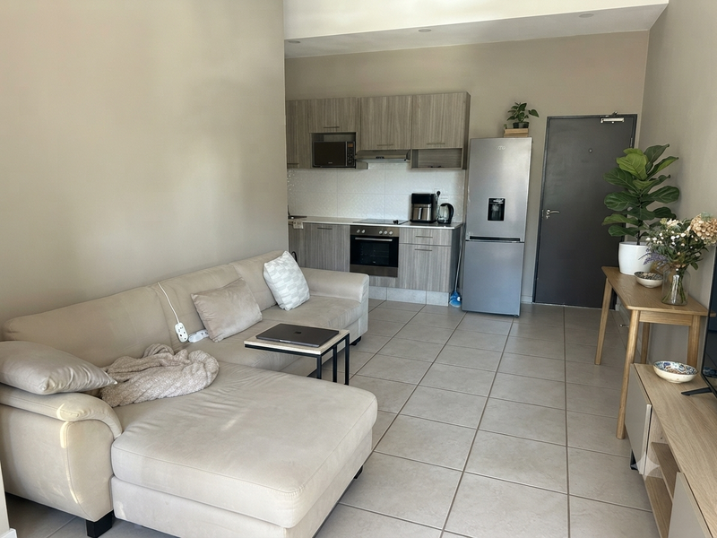 Open-plan living area featuring a modern kitchen with built-in cabinetry, electric hob, oven, and tiled flooring throughout the space.