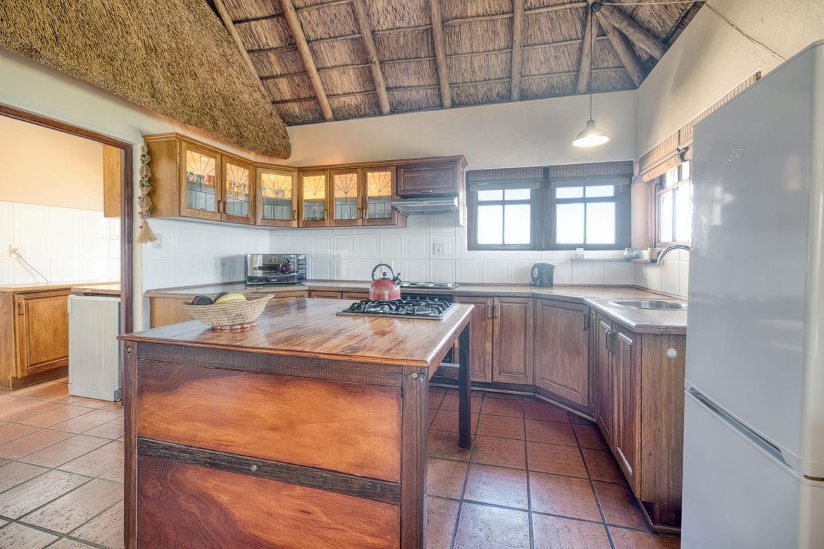 A rustic kitchen featuring a high thatched ceiling, wooden cabinetry, a central island with a built-in gas hob, and tiled flooring.