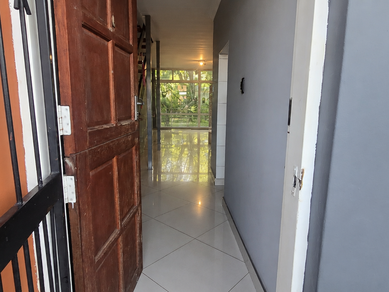 Entrance hallway featuring tiled flooring, a timber front door, and a security gate, leading through to the main living area.
