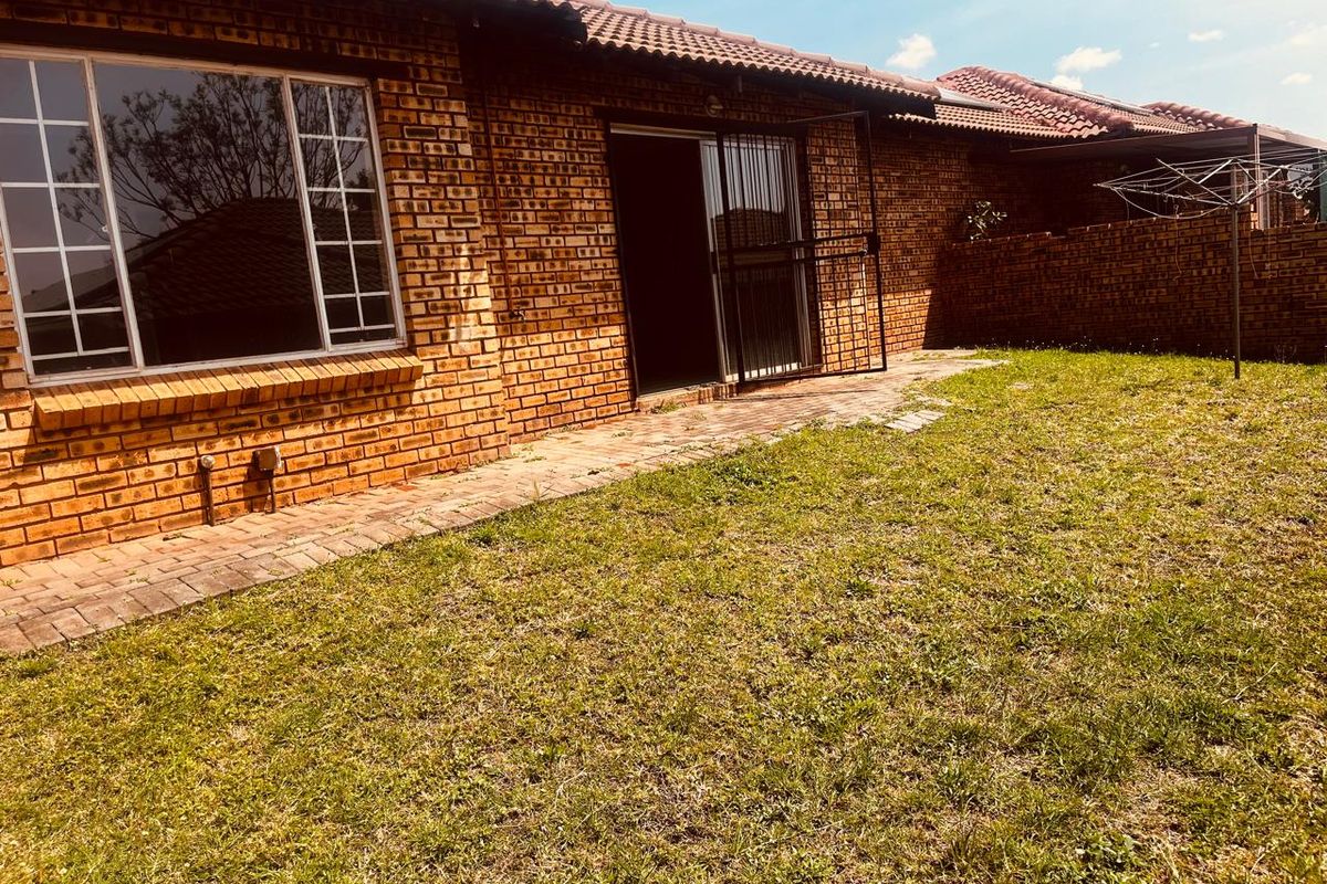 Rear view of a face brick townhouse featuring a paved walkway, sliding door access with security gate, and a private garden area.