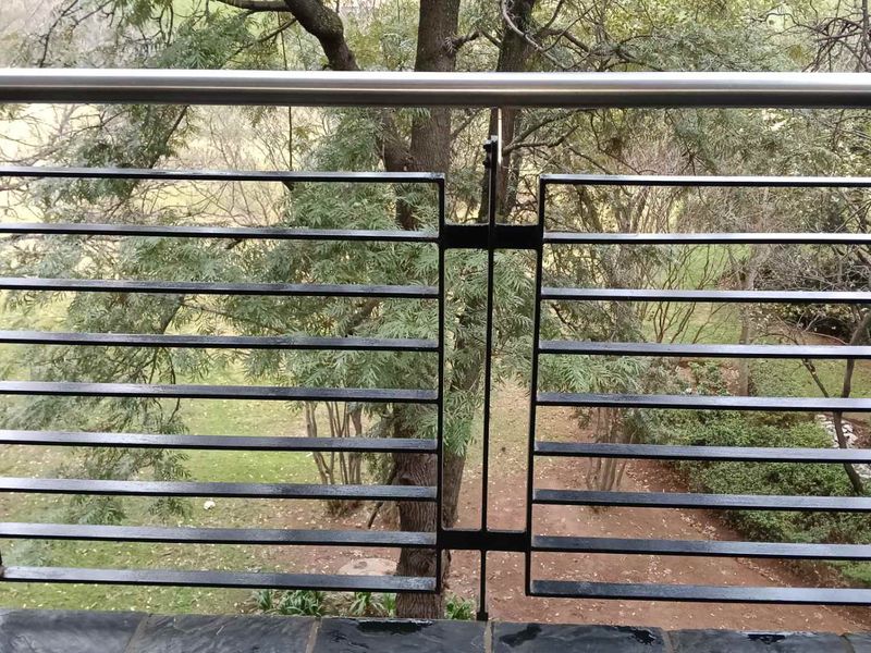 A balcony featuring a modern black metal balustrade with a stainless steel handrail and slate tile flooring, overlooking a garden area.