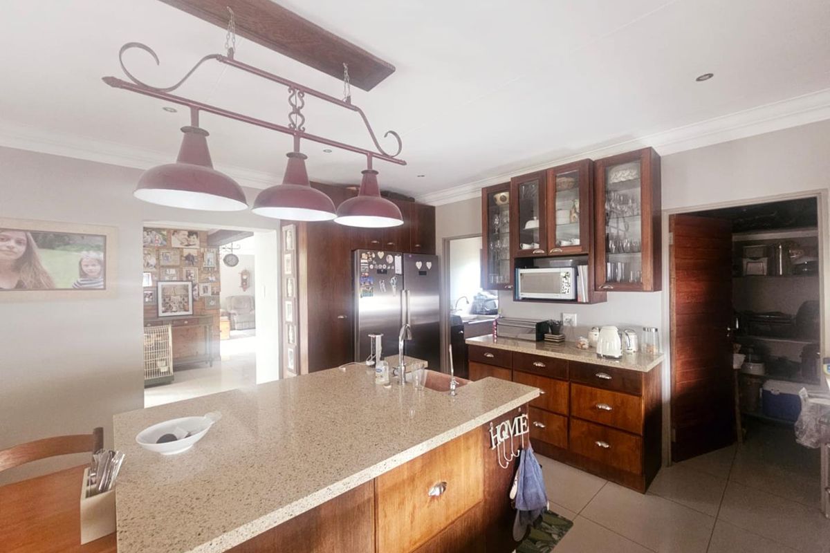 A functional kitchen featuring wooden cabinetry, a central island with a stone countertop, and an adjacent scullery area.