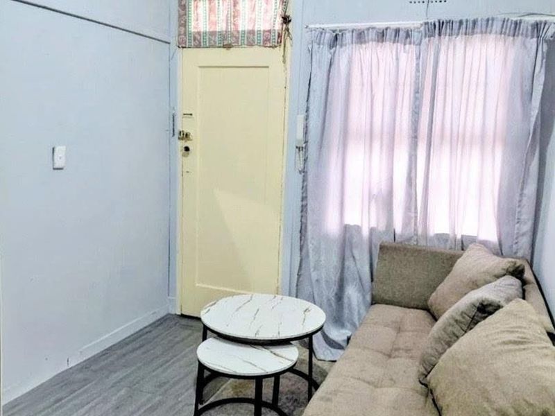 A compact living area featuring light-toned laminate flooring, a traditional timber door with transom window, and a ventilation grille.