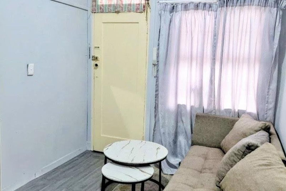 A compact living area featuring light-toned laminate flooring, a traditional timber door with transom window, and a ventilation grille.