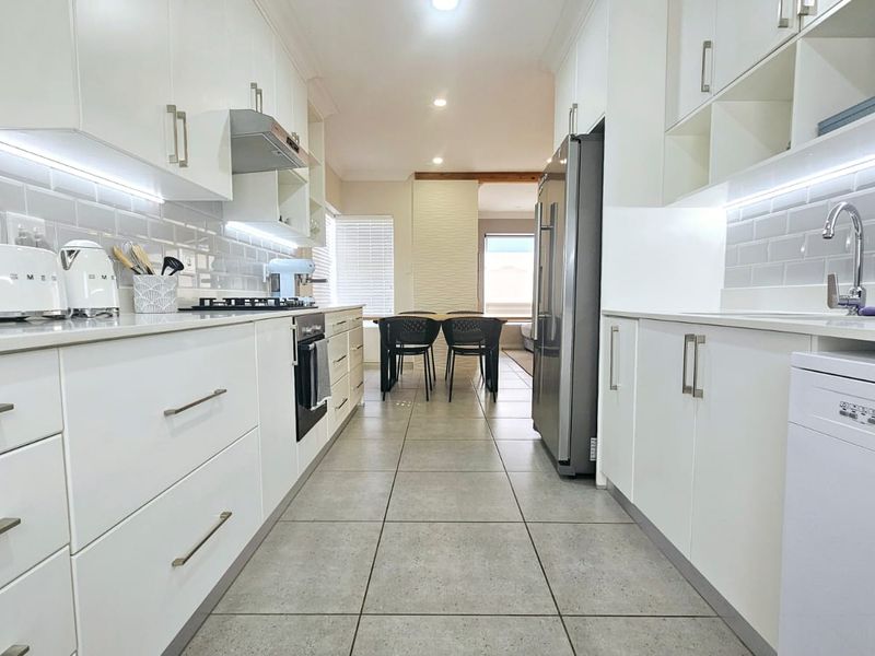 Modern galley-style kitchen featuring white cabinetry, stone countertops, subway tile backsplash, under-cabinet lighting, and high-quality stainless steel appliances.