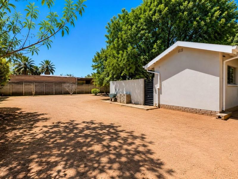 A spacious rear yard featuring a large open area, perimeter walling, and the side elevation of the main dwelling.