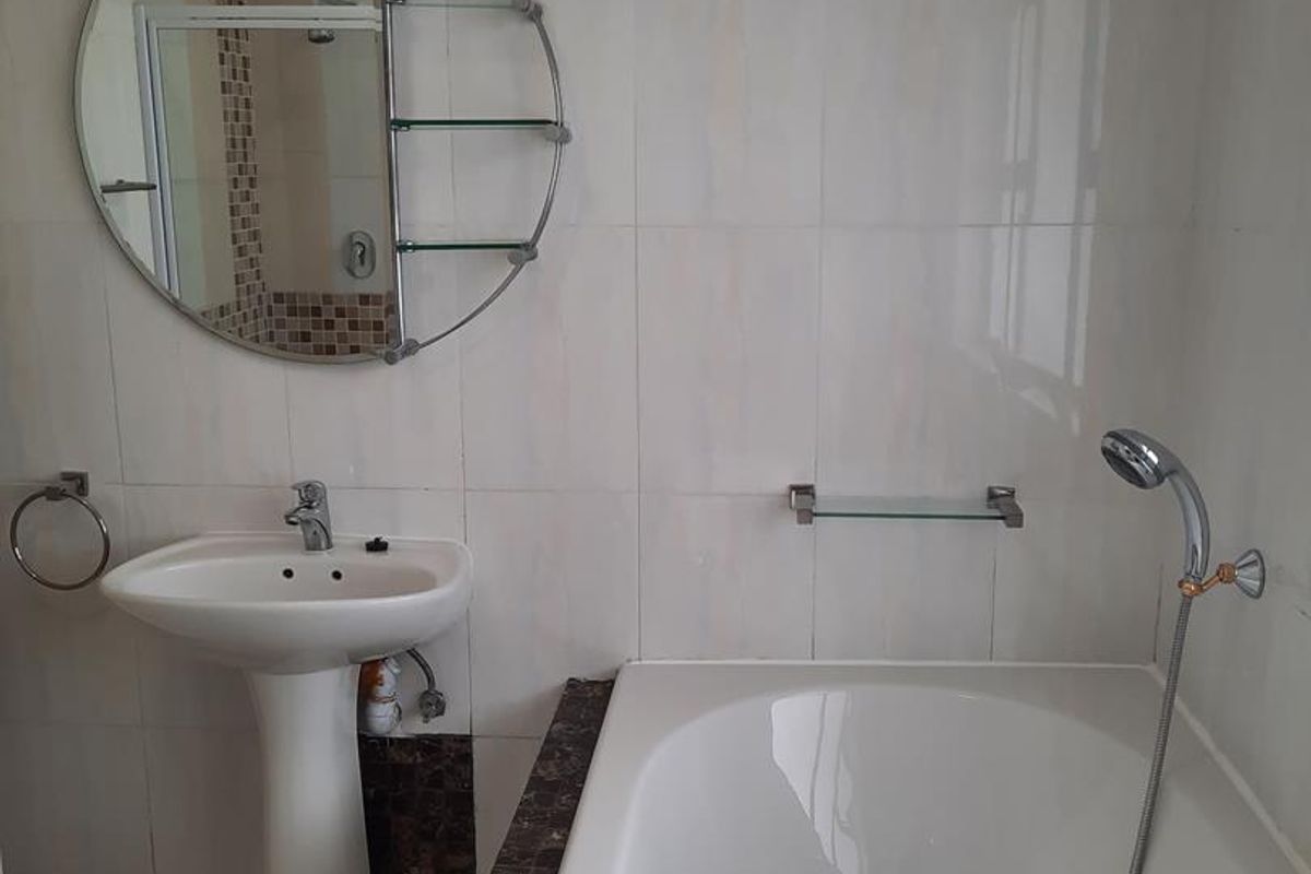 A functional bathroom featuring a white pedestal basin, a built-in bathtub with tiled surround, and a circular wall-mounted mirror with integrated shelving.