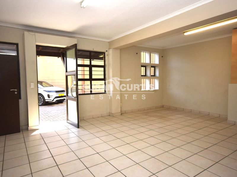 An open-plan industrial space featuring tiled flooring, fluorescent lighting, and direct access to an outdoor area through a security gate.