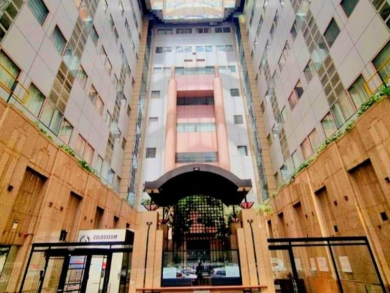 The front entrance of the Colosseum apartment complex, featuring a grand atrium design with stone cladding and modern glass facade elements.