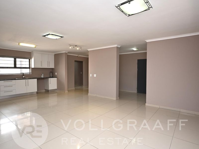 Spacious open-plan living area featuring neutral tiled flooring, modern kitchen cabinetry, and recessed ceiling lighting, offering a versatile and bright layout.