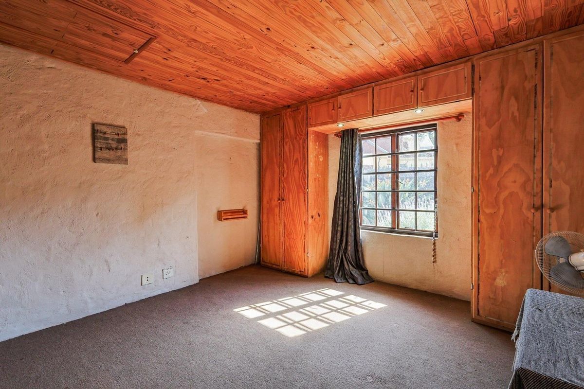 A bedroom featuring built-in wooden cabinetry, a timber-paneled ceiling, and a window with security bars.