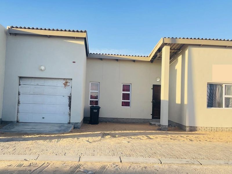 Front elevation of a single-story house featuring a single garage, paved driveway, and neutral exterior walls with security bars on windows.