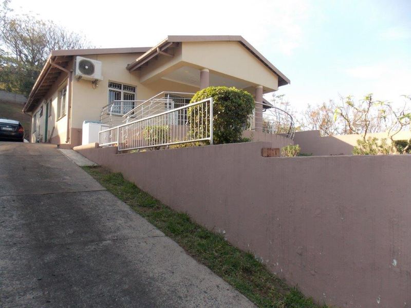 Front exterior view of the house featuring a concrete driveway, retaining wall, covered porch, and security bars on the windows.