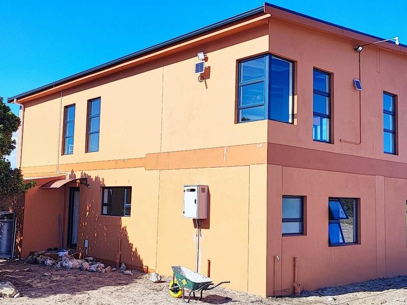 A two-story farm dwelling featuring modern orange exterior walls, aluminium window frames, a gas geyser, and an upper-level balcony with surrounding natural landscape.