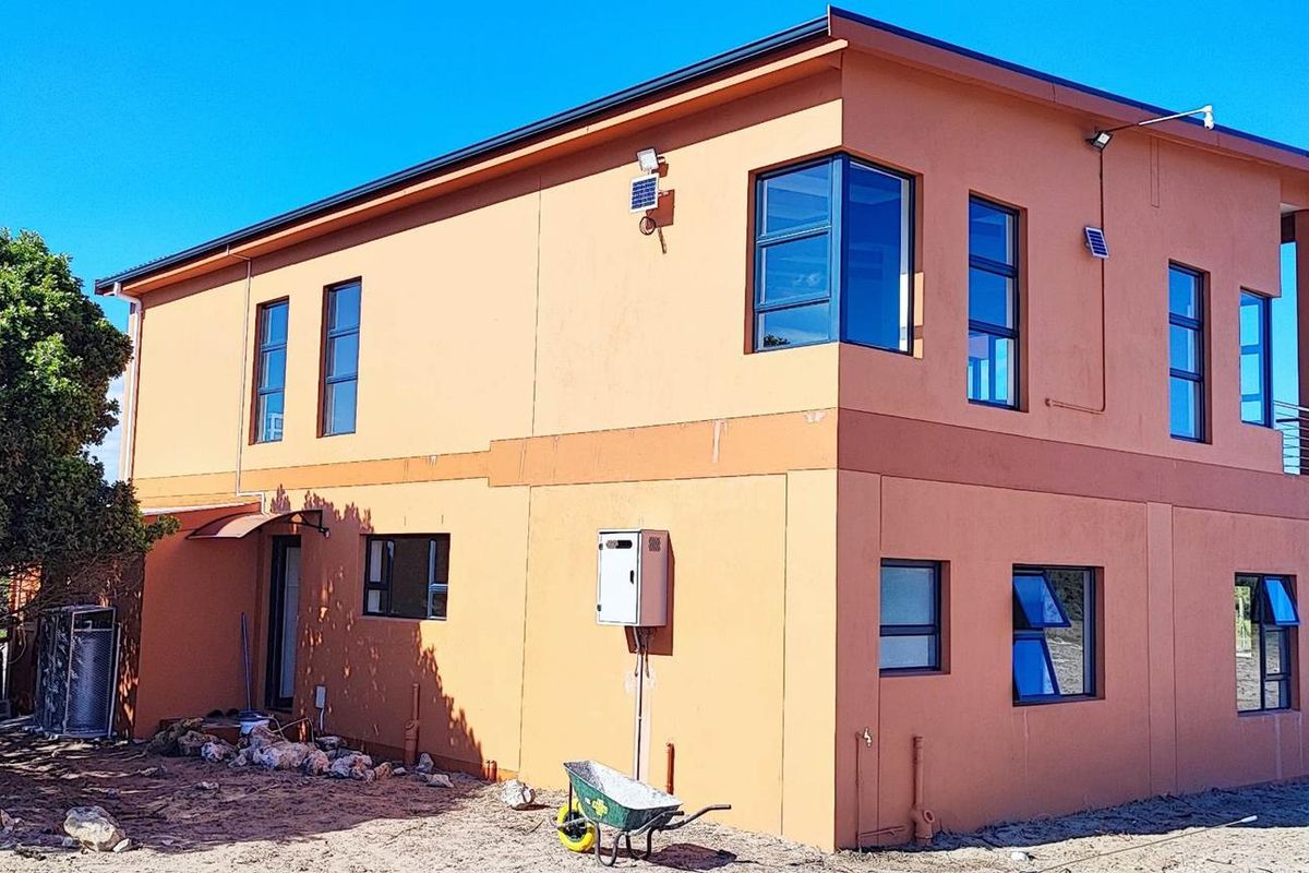 A two-story farm dwelling featuring modern orange exterior walls, aluminium window frames, a gas geyser, and an upper-level balcony with surrounding natural landscape.
