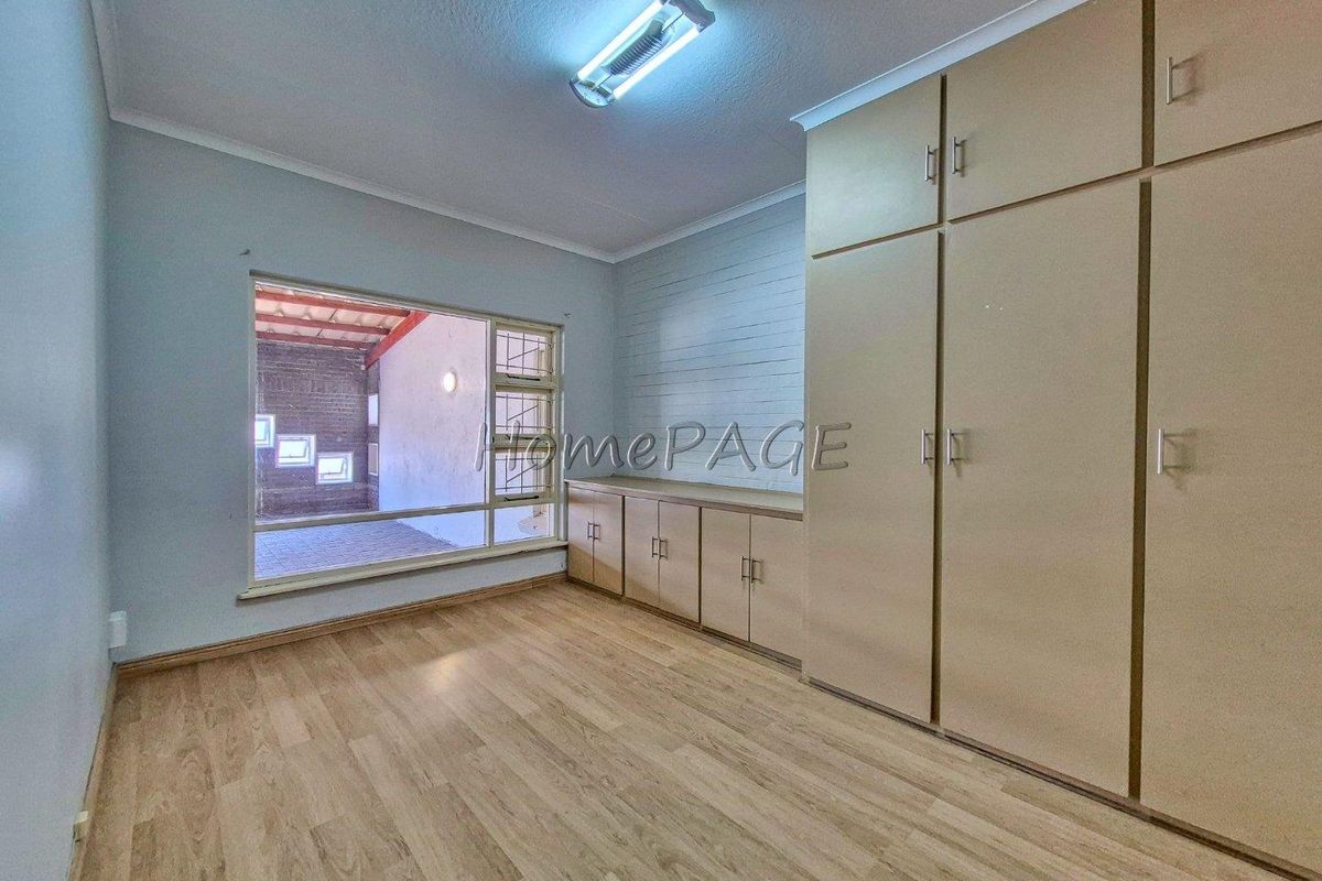 A bedroom featuring built-in wooden cabinetry, laminate flooring, and a large window overlooking an enclosed patio area.