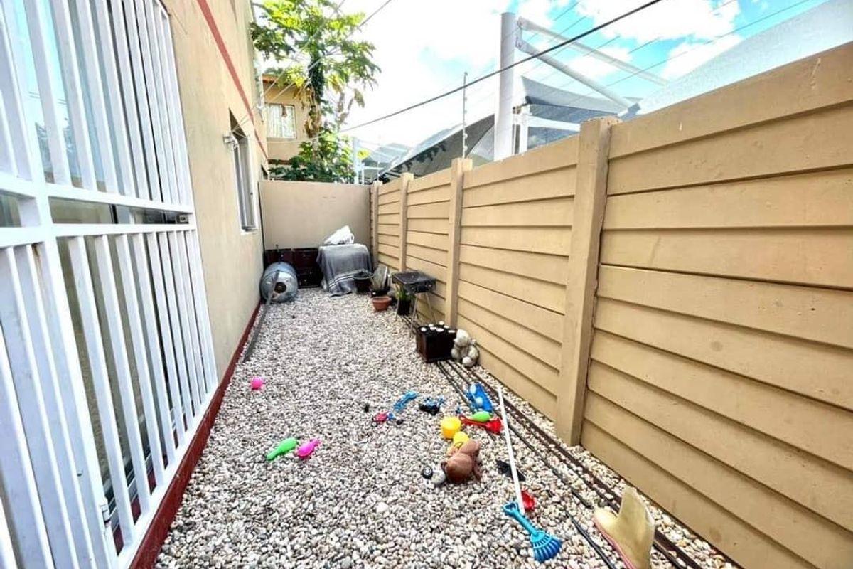 A narrow side yard or exterior passage featuring a gravel ground cover and a precast concrete boundary wall.