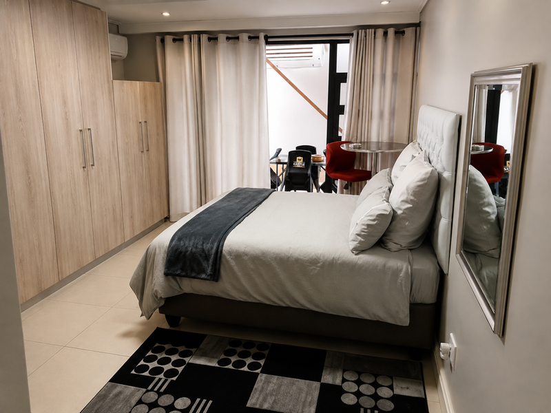 A well-maintained bedroom featuring built-in wooden cupboards, tiled flooring, recessed lighting, and direct access to a private balcony through sliding glass doors.