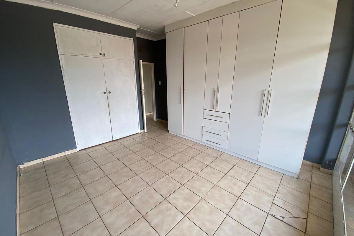 A bedroom featuring tiled flooring, built-in cupboards, and a secondary storage closet, offering a functional space with neutral wall tones.