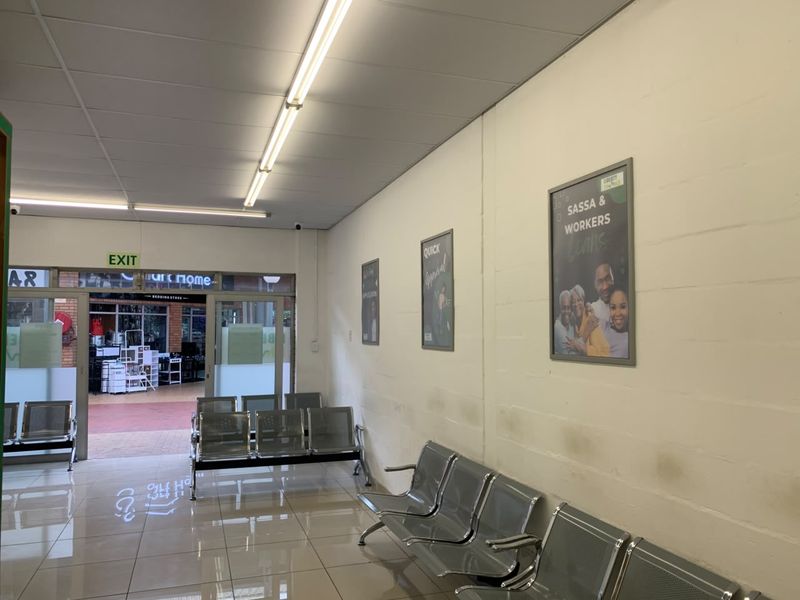 A functional retail entrance area featuring tiled flooring, fluorescent lighting, and a glass door leading to an exterior walkway.