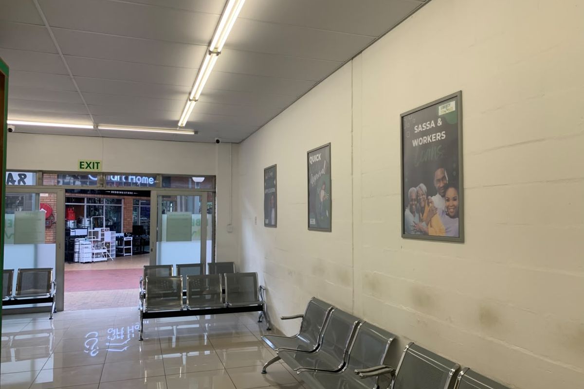 A functional retail entrance area featuring tiled flooring, fluorescent lighting, and a glass door leading to an exterior walkway.