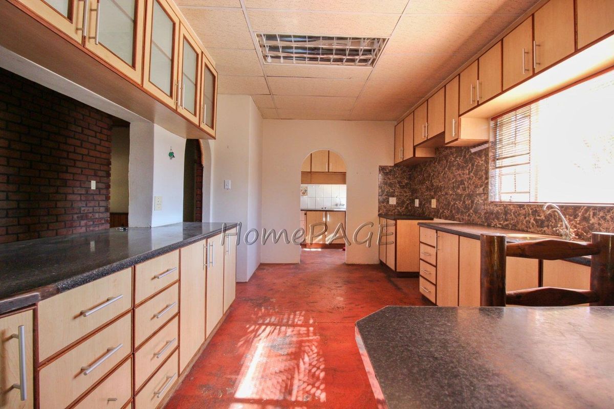 Spacious kitchen featuring extensive built-in cabinetry, laminate countertops, and a brick feature wall, offering significant potential for a modern renovation.