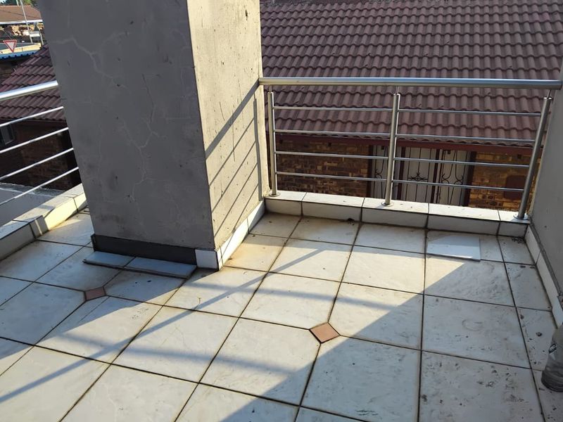 An outdoor balcony featuring tiled flooring and a stainless steel balustrade, currently showing signs of wear and requiring maintenance on the pillar and floor tiles.