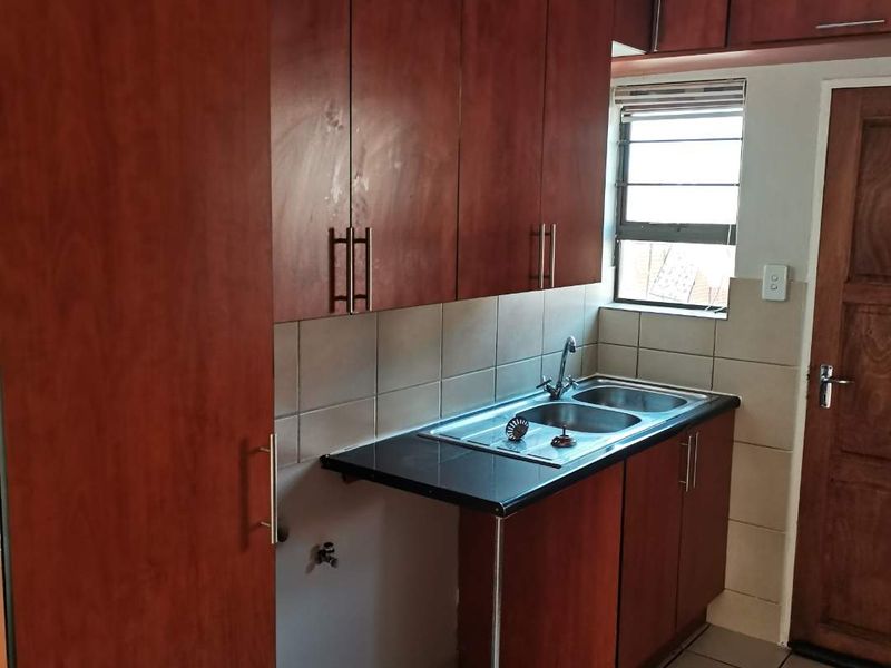 A compact kitchen featuring wood-look laminate cabinetry, a double bowl stainless steel sink, tiled backsplash, and ceramic floor tiles.