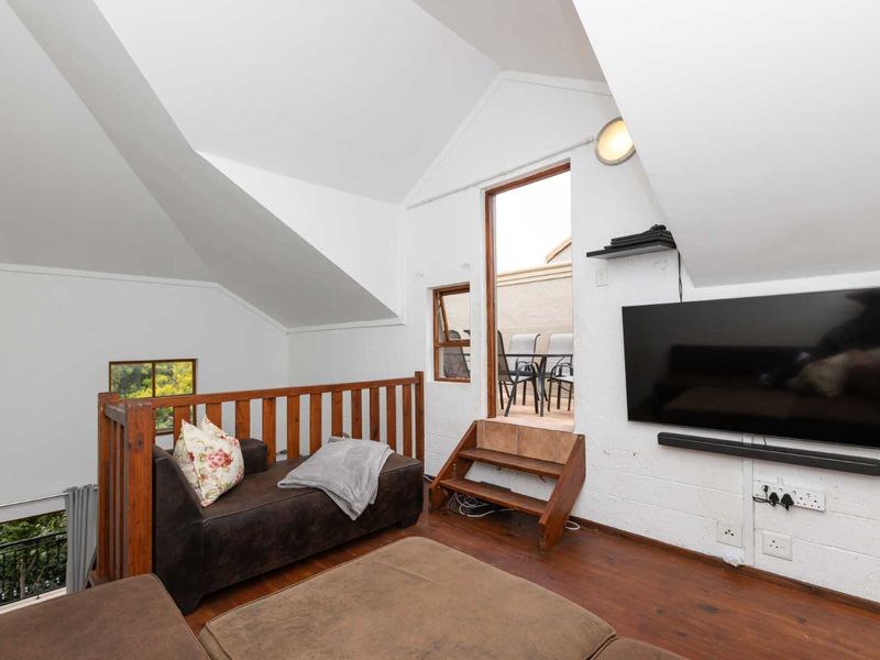 A cozy attic-style living room featuring vaulted ceilings, timber flooring, and direct access to an outdoor balcony area.