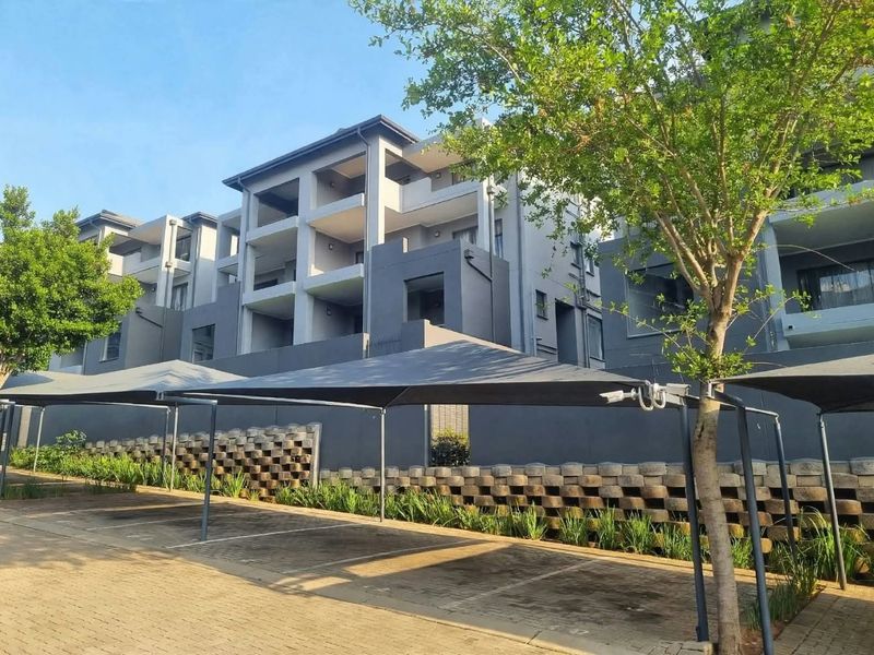 Exterior view of the apartment complex featuring covered parking bays, a retaining wall, and multi-level balconies.