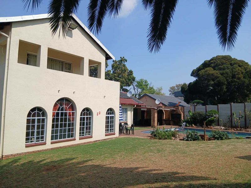 Rear view of a double-story house featuring a swimming pool, covered patio with built-in braai, and a spacious garden with boundary walling.