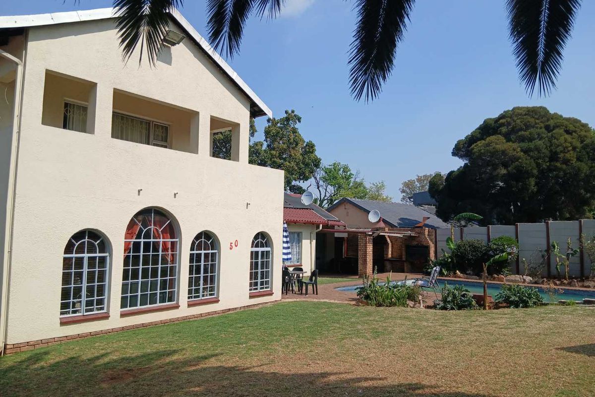 Rear view of a double-story house featuring a swimming pool, covered patio with built-in braai, and a spacious garden with boundary walling.