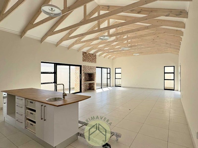 Spacious open-plan living area featuring exposed timber trusses, a modern kitchen island, and a built-in brick fireplace with large sliding doors.