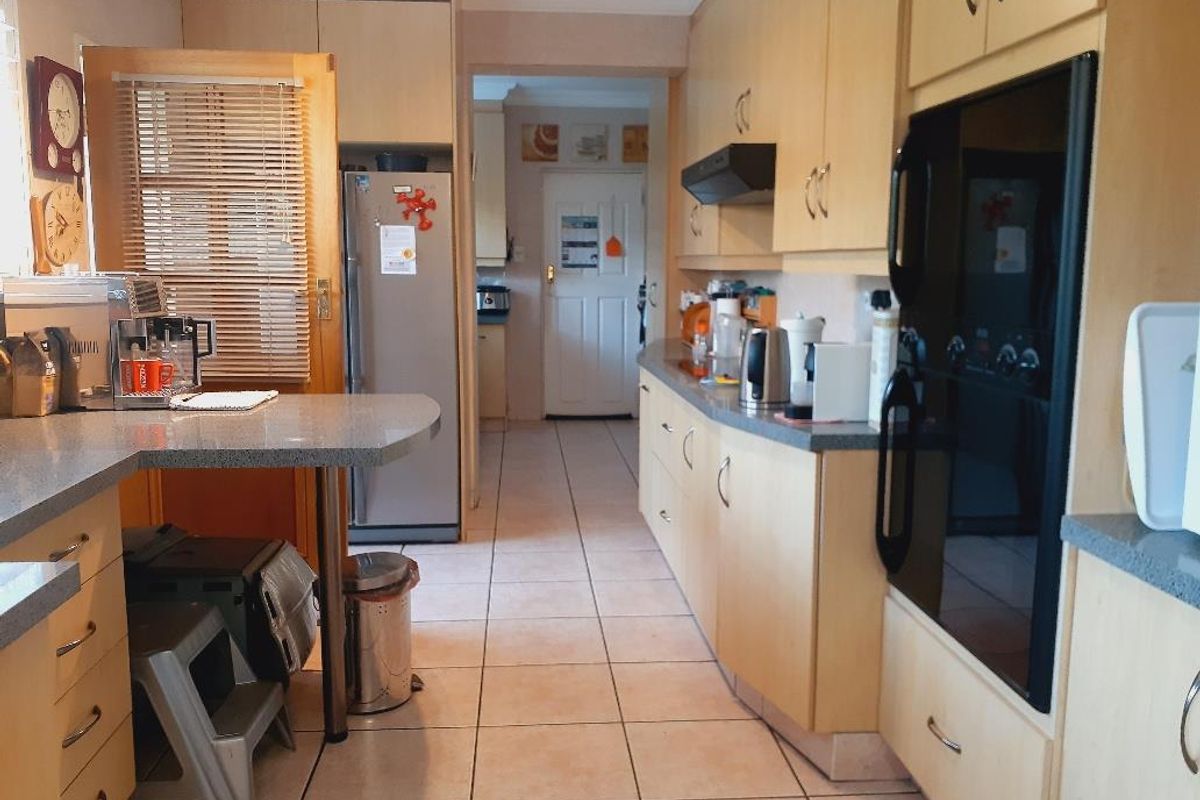 A functional kitchen featuring light wood cabinetry, stone-look countertops, built-in oven, and tiled flooring, with an open layout leading to an adjacent utility area.