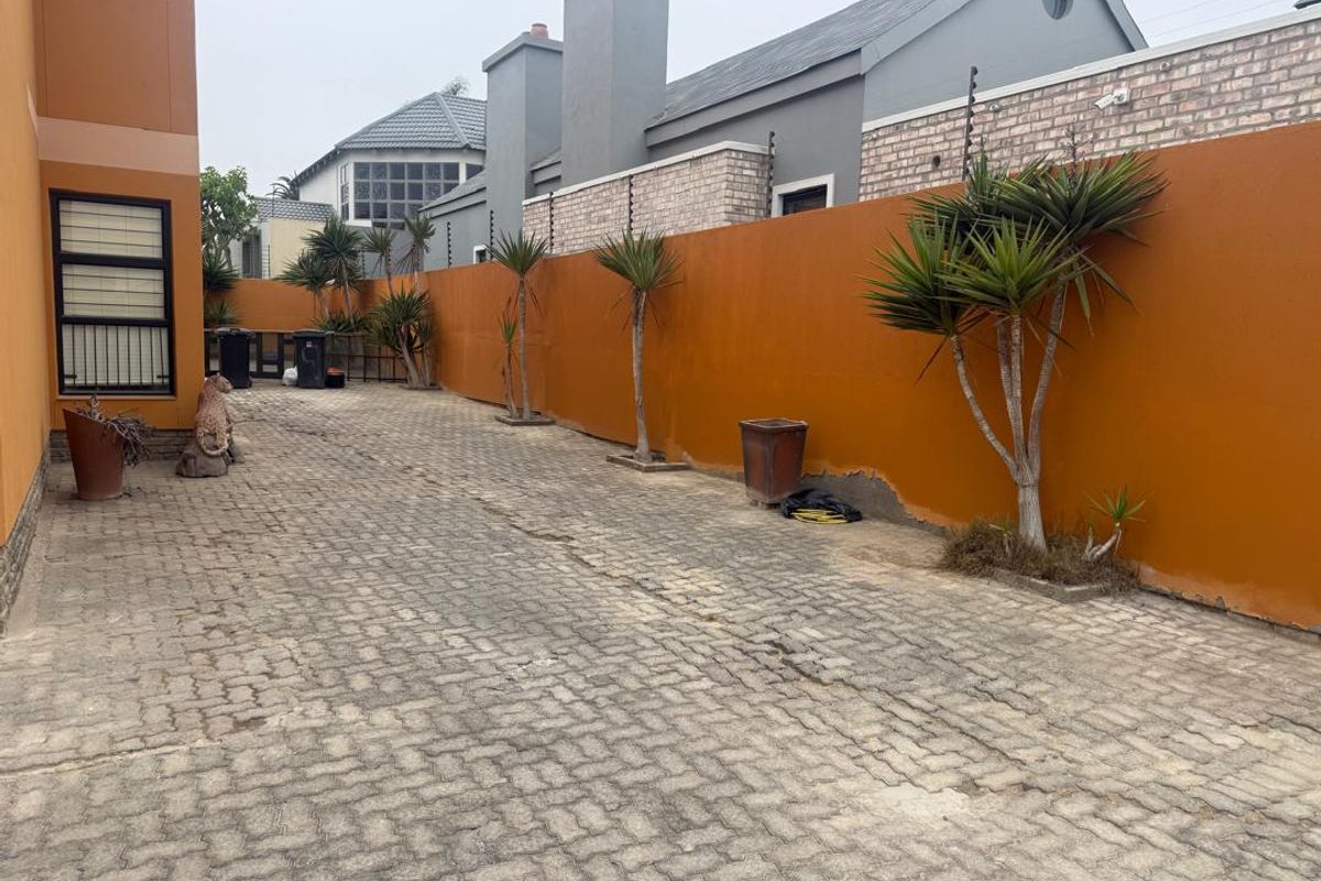 A paved side or rear yard area featuring a high boundary wall with electric fencing and security bars on the adjacent building windows.