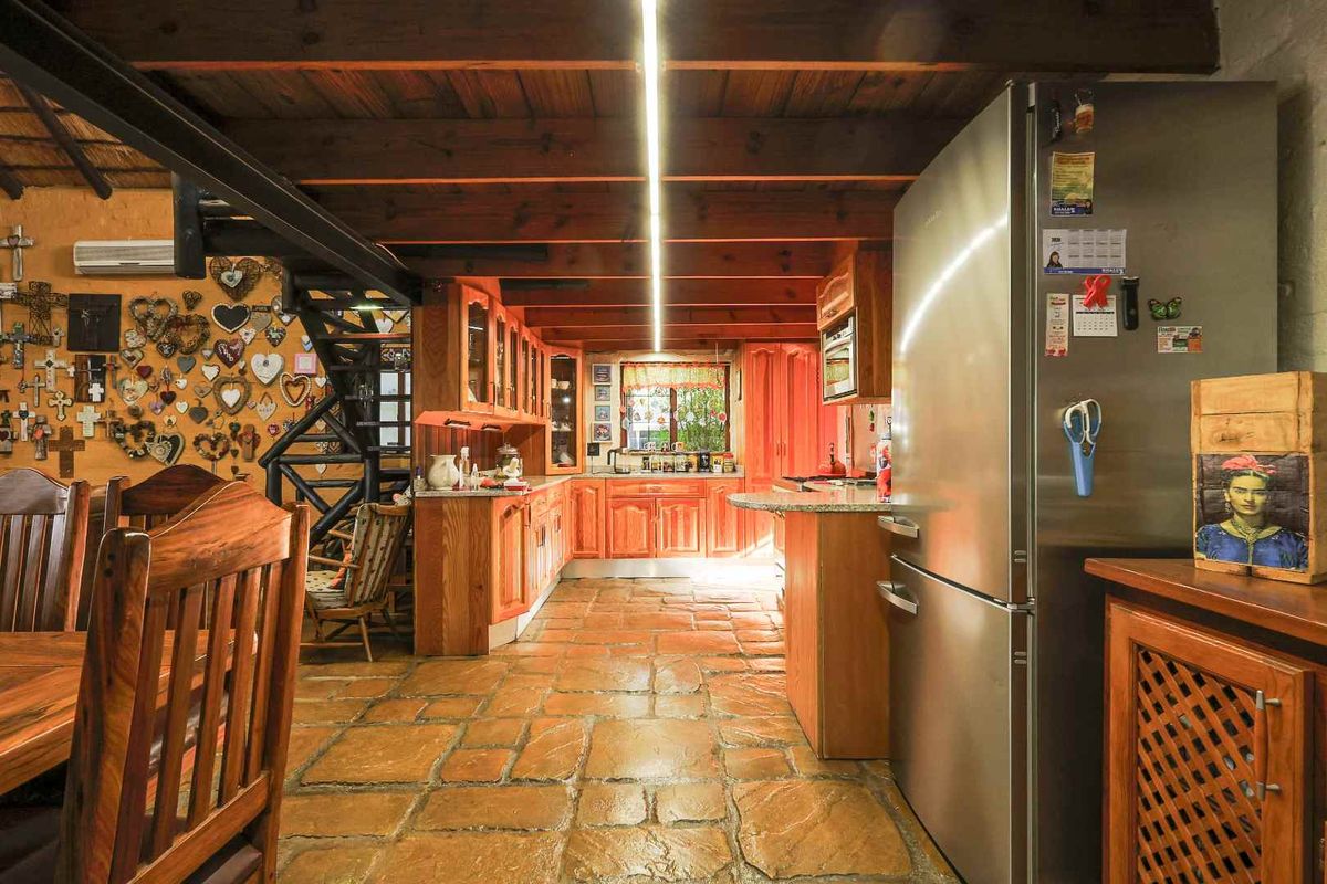 Rustic kitchen featuring exposed timber ceiling beams, stone tile flooring, and warm wooden cabinetry with granite countertops.