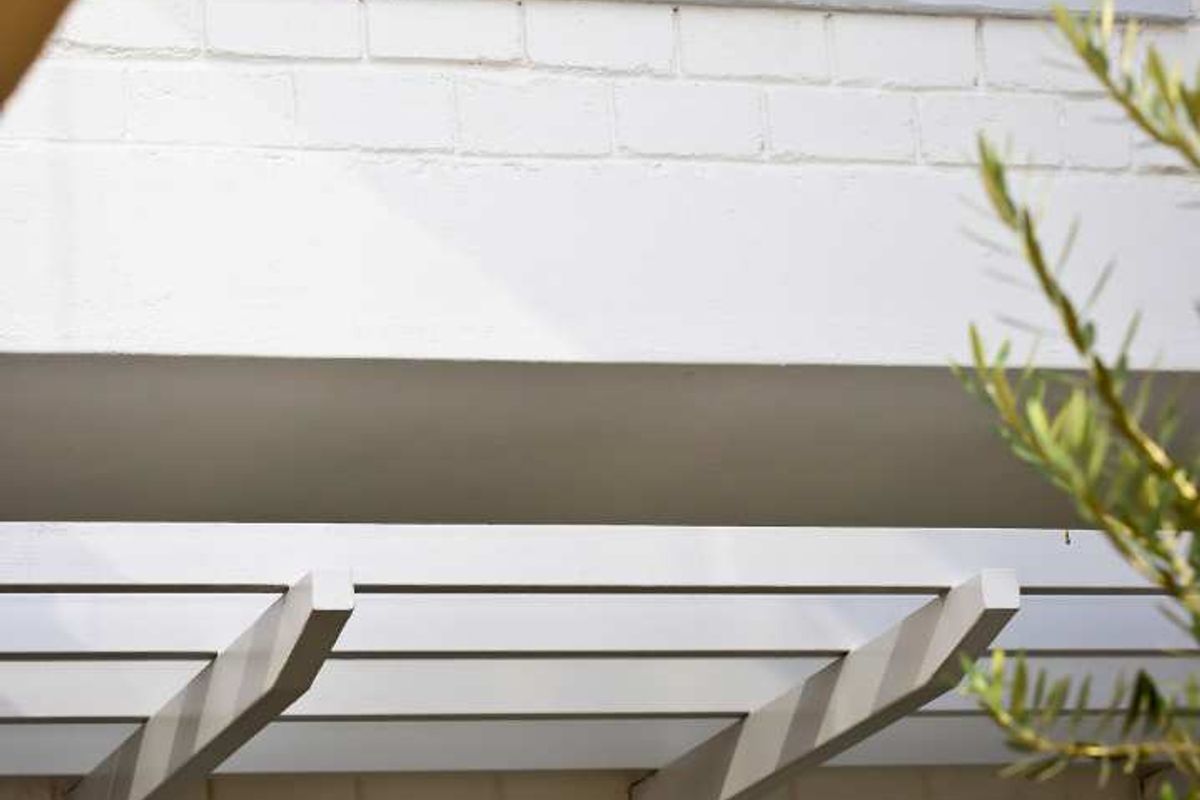 A close-up view of the penthouse exterior featuring painted brickwork, a modern pergola structure, and dark-framed windows with integrated shutters.