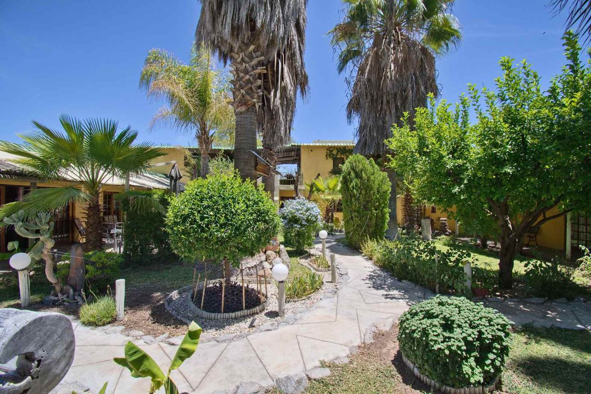 A lush, landscaped garden courtyard featuring a stone pathway, mature palm trees, and established greenery surrounding the guest house exterior.