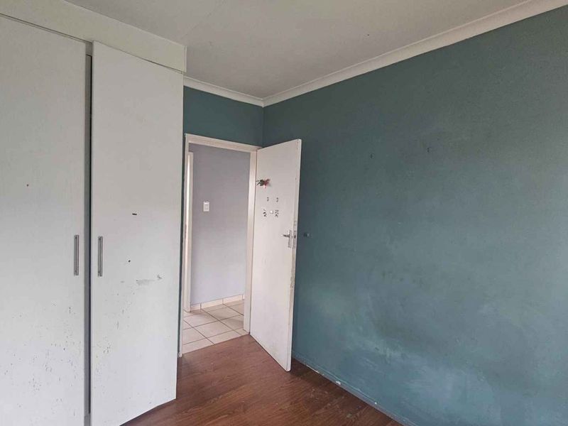 An empty bedroom featuring laminate flooring, a built-in wardrobe, and a coved ceiling, requiring cosmetic updates to the wall paint and finishes.