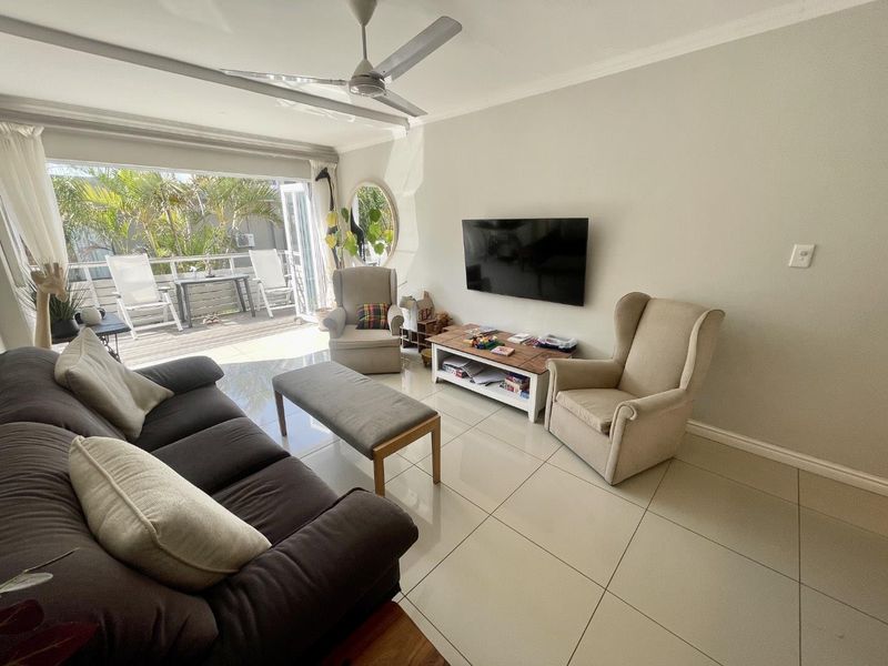 A bright, open-plan living room featuring large format floor tiles, a ceiling fan, and seamless access to an outdoor patio through sliding glass doors.