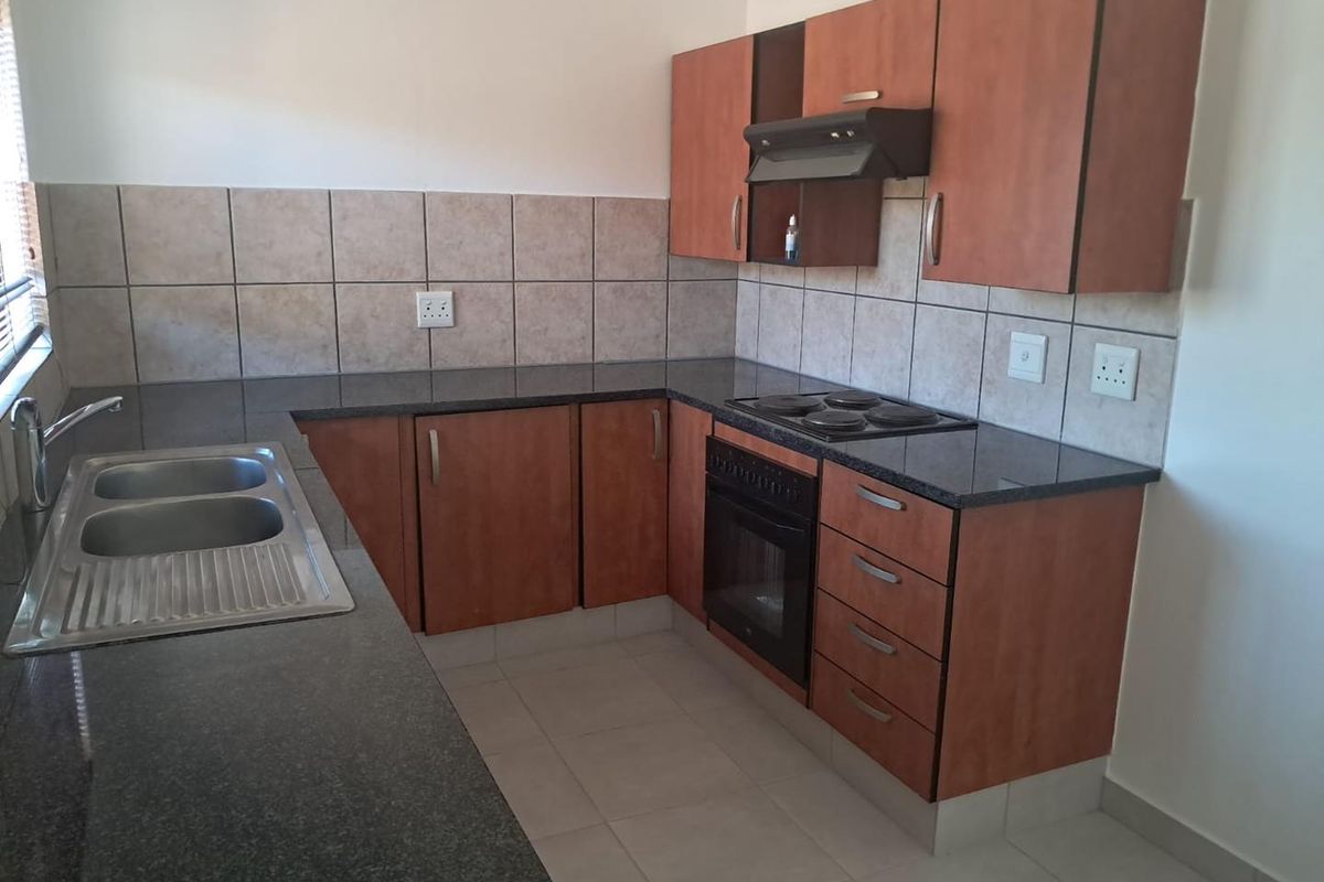 A functional kitchen featuring laminate cabinetry, granite countertops, a built-in oven with hob, and a stainless steel double sink with tiled splashbacks.