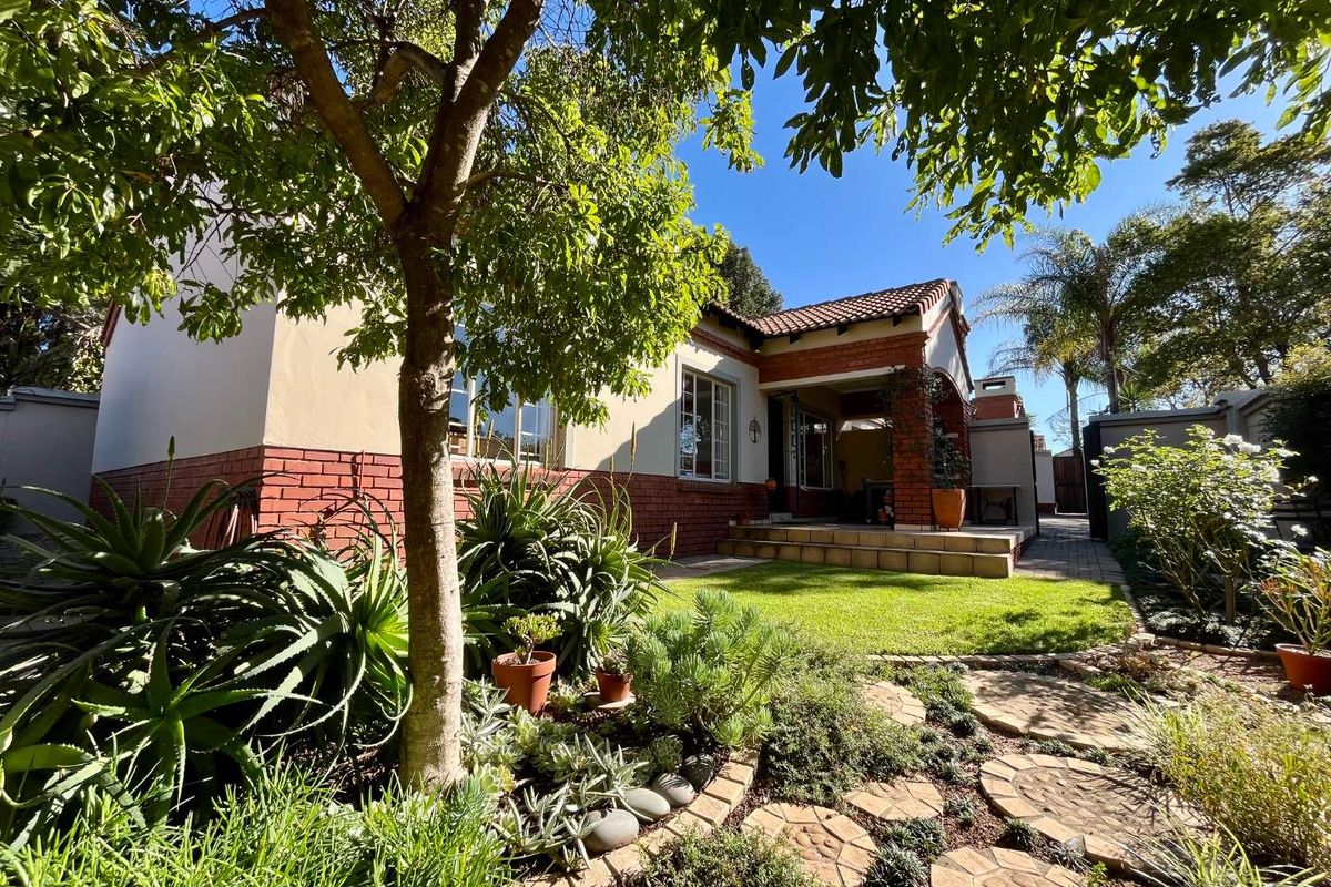 A charming townhouse exterior featuring a red brick and plaster facade, a covered patio entrance, and a well-maintained landscaped garden with mature trees.