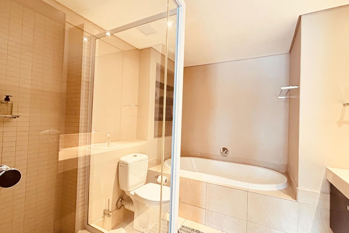 Modern bathroom featuring a glass-enclosed shower, a built-in bathtub, and a vanity with neutral tiling throughout.