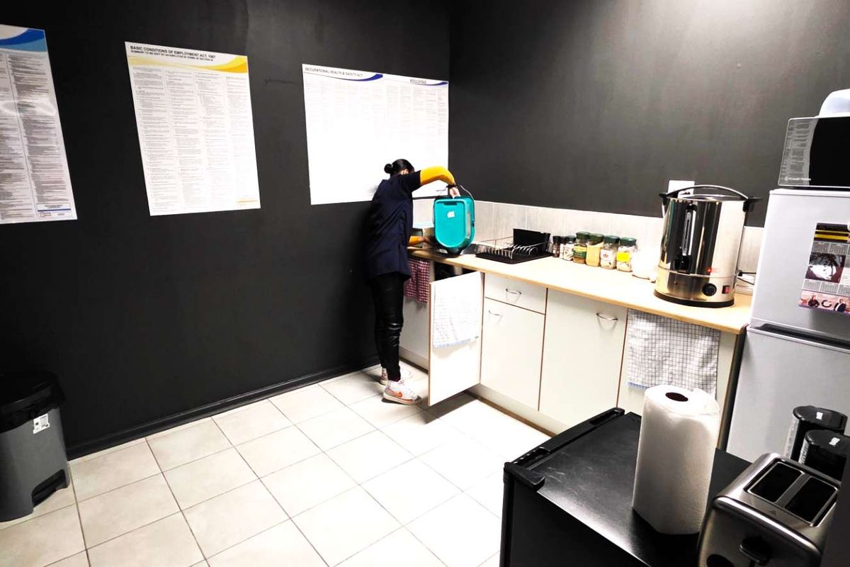 A functional office kitchenette featuring white cabinetry, tiled flooring, and dark painted walls, providing a practical space for staff refreshments.