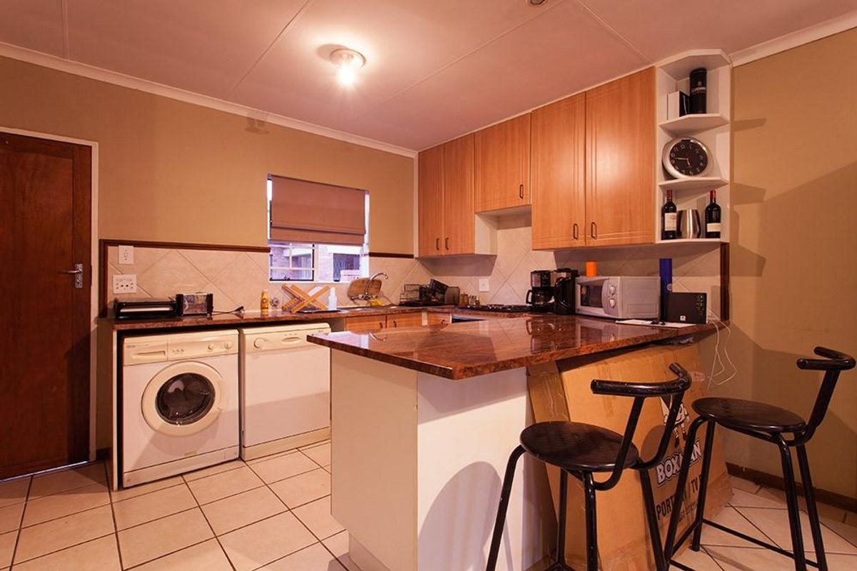 Functional kitchen featuring wood-look cabinetry, granite-style countertops, tiled flooring, and integrated space for laundry appliances.