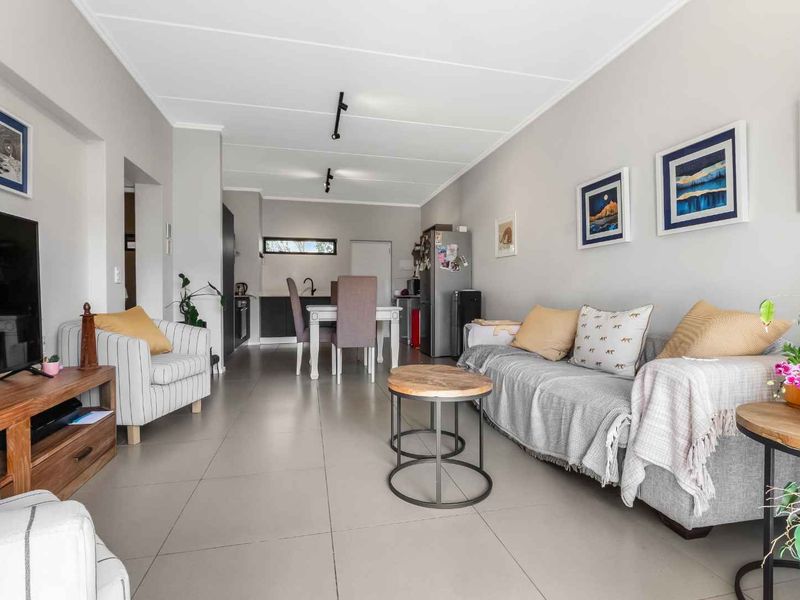 A bright open-plan living and dining area featuring neutral tiled flooring and modern recessed ceiling lighting, creating a spacious and functional layout.