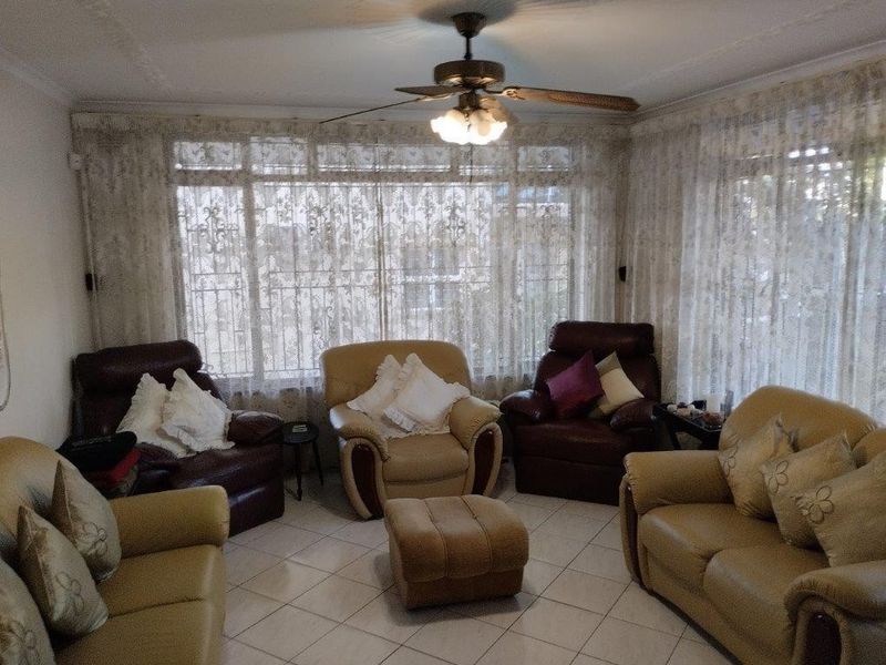 A living room featuring tiled flooring, a ceiling fan, and large windows with decorative curtains, providing a functional and well-lit space.